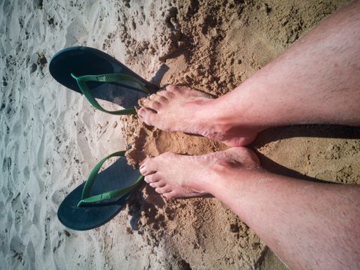A vertical shot of sunburned feet with flip flops on the beach