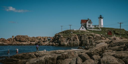 A scenic view of the Nubble Lighthouse in Maine on blue sky background and people on the rocks