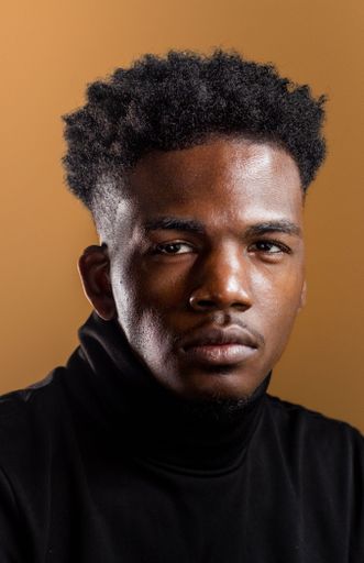 A vertical shot of an African American man on the ochre color background.