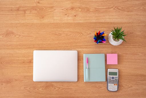 A top view of work and study essentials including a laptop, calculator, notebook on a wooden table