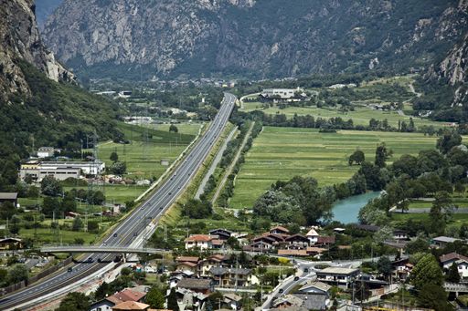 A road surrounded by buildings and mountains covered in greenery in the countryside at daytime