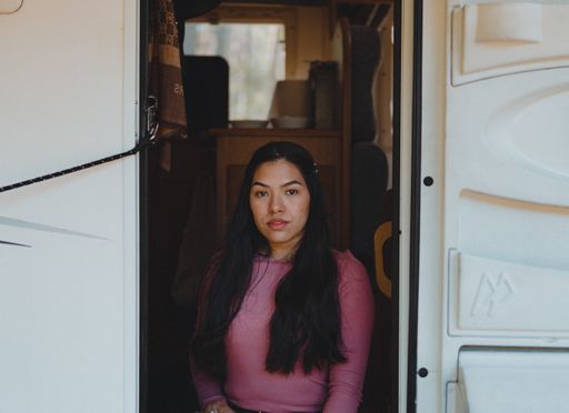 A woman with pink blouse and long hair sitting on the stairs of the bus