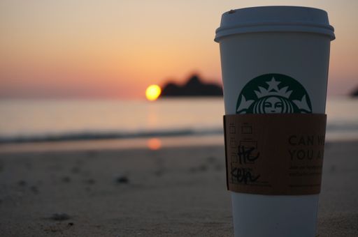 A closeup shot of a Starbucks paper cup at sunset at Lanikai Beach, Oahu, Hawaii