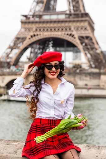 A vertical shot of a Hispanic girl wearing red tones holding tulips sitting by the Eiffel Tower