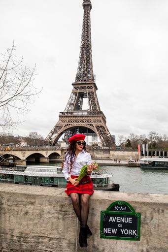 A vertical shot of a Hispanic girl wearing red tones holding tulips sitting by the Eiffel Tower