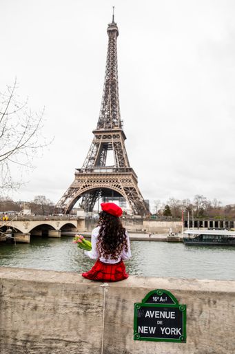 A vertical shot of a Parisian woman holding tulips sitting by River Seine next to the Eiffel tower