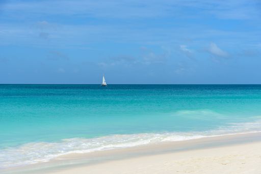 A horizontal shot of the mesmerizing view of the beach and sea, with a sailboat in the distance  -perfect for wallpaper
