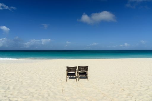A horizontal shot of the mesmerizing view of the beach and sea, with two empty chairs on the shore -perfect for wallpaper