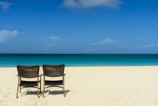 A horizontal shot of the mesmerizing view of the beach and sea, with two empty chairs on the shore -perfect for wallpaper