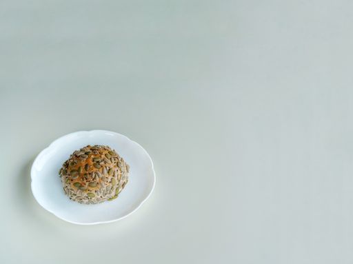 An overhead shot of bread with pumpkin and sunflower seeds on a white plate under the light