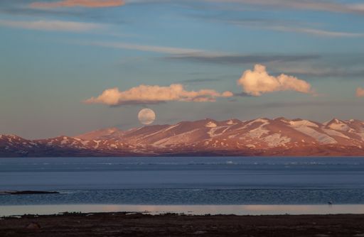 A mesmerizing view of the full moon over snowy mountains with the sea