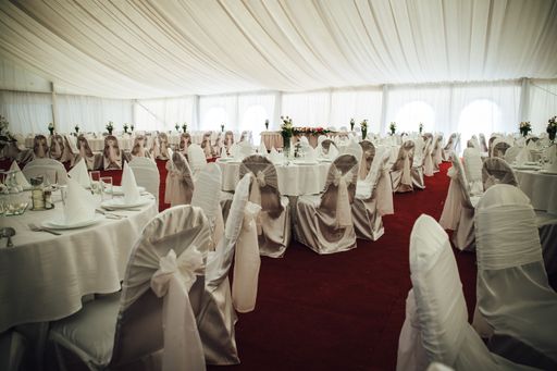 A Wedding hall surrounded by white decorated tables and chairs on a red floor