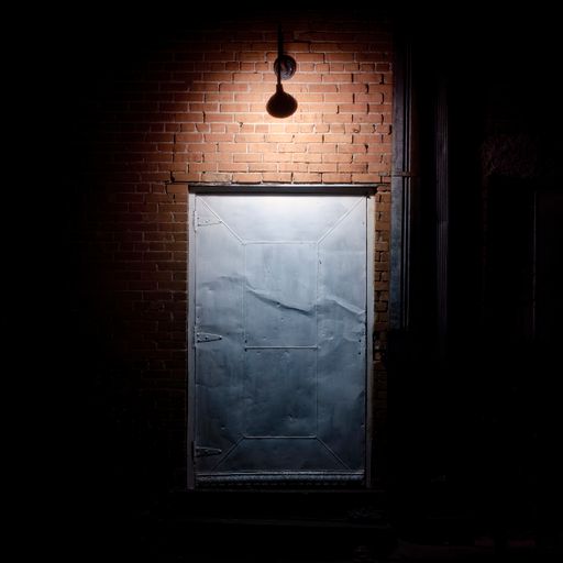 View from the alley at night of an old theater built in the 1940s. The single light breaks the darkness and highlights the brick wall