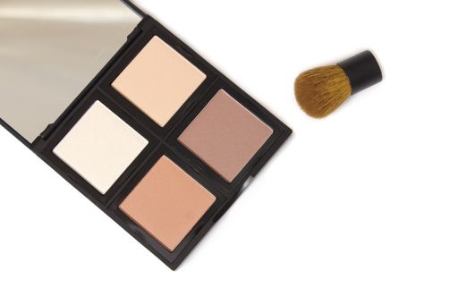 A closeup of a cosmetic palette and brush on white background. Contour and highlighter.