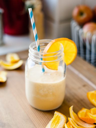 Banana orange smoothie in a glass jar with a blue paper straw, food photography, healthy drink