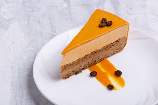 A closeup shot of a slice of yellow-layered cake topped with roasted coffee beans on a white plate