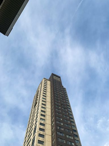 A vertical shot of a modern high rise building against a blue cloudy sky