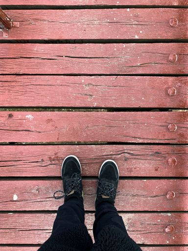 A vertical shot of the legs of a man standing on a wooden deck