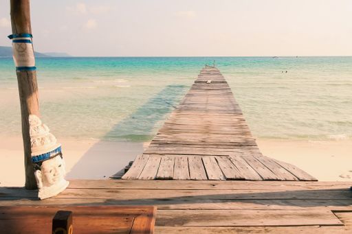 A scenic view from a gazebo of a wooden boardwalk leading to the white sandy beach of Koh Rong Sanloem