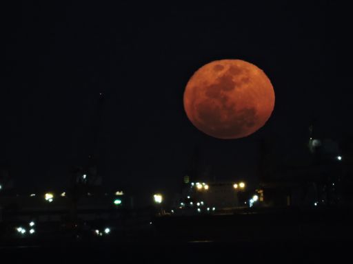 A shot of a yellow supermoon with a foreground of a cargo ship and body of water