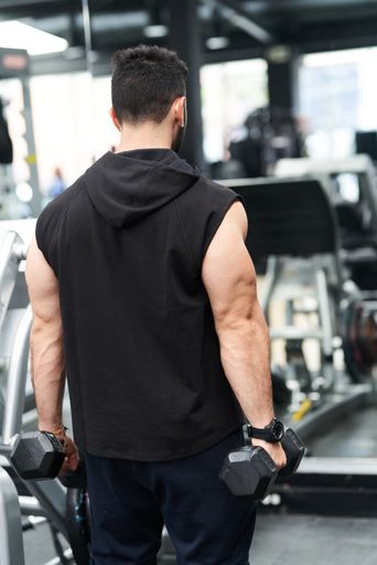 A vertical shot of a the back of a man working out with dumbbells in a gym
