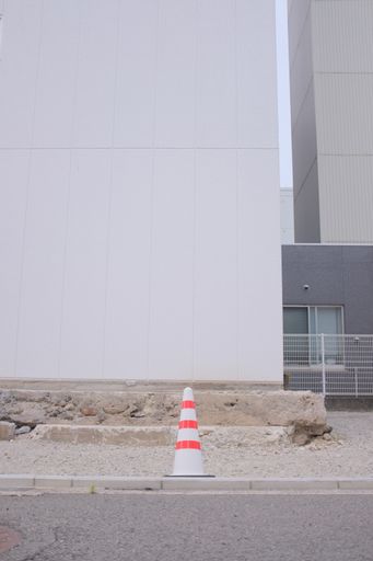 A vertical shot of a traffic cone against a white building near the road