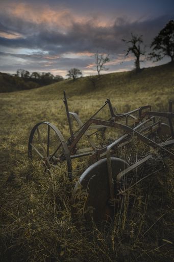 A vertical shallow focus shot of an old rusty vintage bike in a green field with beautiful cloudy sky during sunset