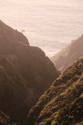 A vertical aerial shot of the mountains with roads with ocean in the background