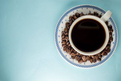 A top view of a cup of black coffee and beans on a blue background
