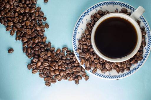 A top view of a cup full of coffee and coffee beans on a blue background