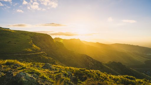 A scenic view of the mountains covered in greenery under the sunlight at sunset in Christchurch, New Zealand