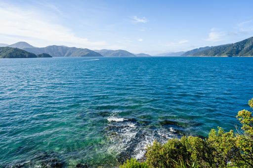 A Beautiful shot of sea water surrounded by green hills and mountains under a blue sky