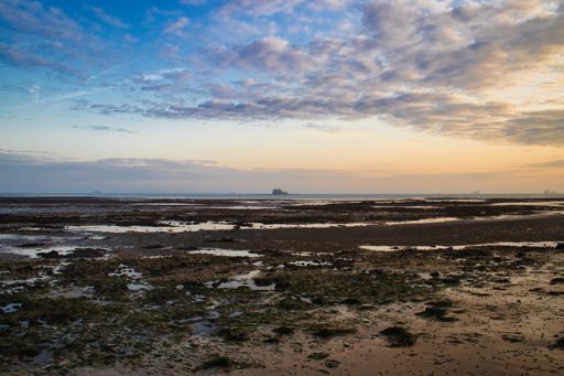 A landscape view of a sunrise over the beach at low tide against a clouded sky