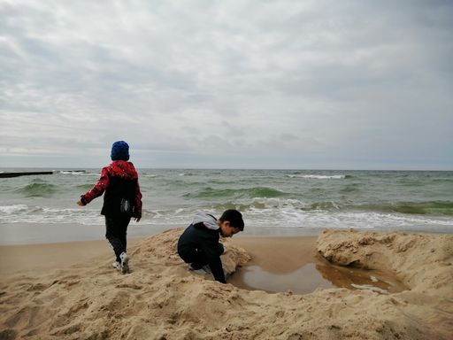 Two kids playing with sand close by the water at a beach
