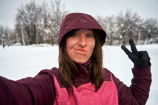 A closeup of a Caucasian female taking a selfie outdoors in the wintertime while holding a peace sign