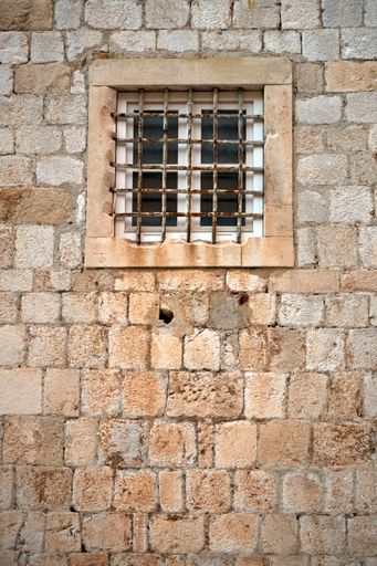 A vertical shot of building wall with window in front of window bars