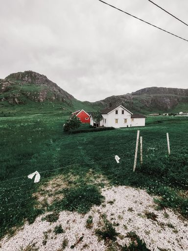 A vertical shot of a wooden house with farm and hangar in the field in foot of mountains