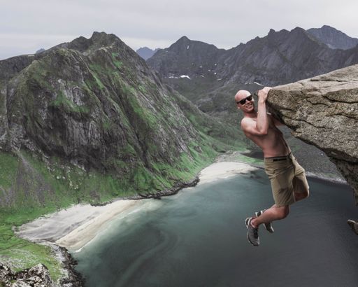 A aerial shot of a man hanging on a rock cliff overlooking a sea - concept of don't give up