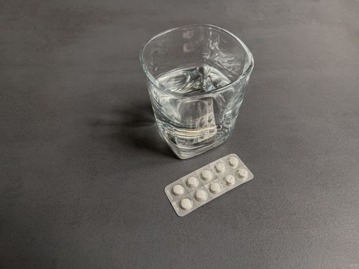 A closeup shot of a glass of water with drug pills on a gray table surface