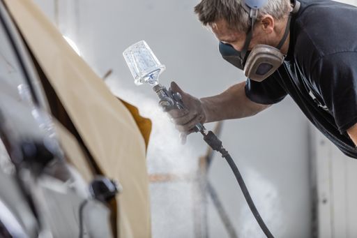 A shallow focus of a man spray painting a car in spray-painting booth