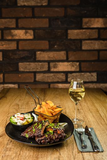 A vertical shot of a steak dinner with village fries, a fresh salad, cutlery and white wine in a glass