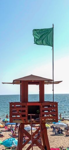 A wooden lifeguard tower with a green flag on a beach