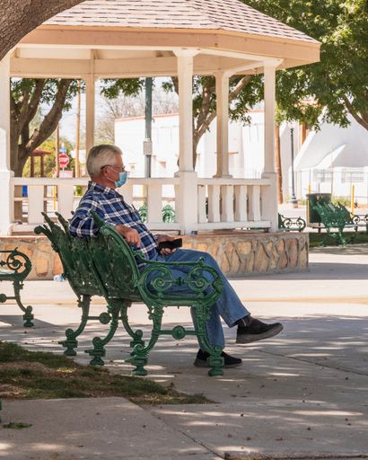 A vertical shot of a senior man in a medical mask sitting on a bench.