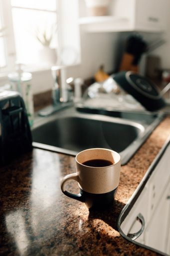A vertical closeup shot of the hot coffee in the kitchen with sunlights coming from a window