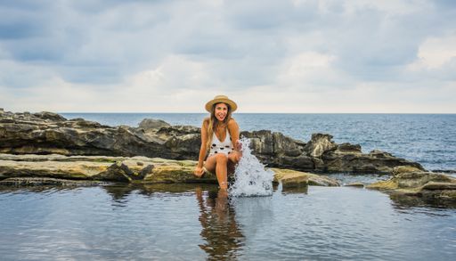 A young female in a swimsuit with dots sitting on a rock near the sea