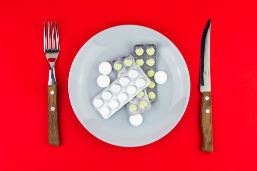 A top view of a table setting with a plate full of pills on a red background