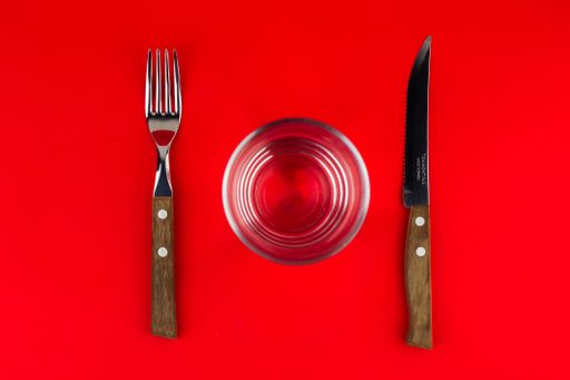 A top view of a fork, a glass cup and a knife on a red background