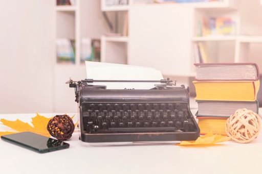 Workplace of a writer or correspondent: an old typewriter, a mobile phone, a stack of books and two yellow dry maple leaves