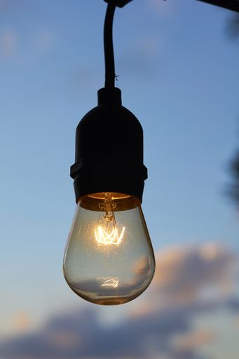 A vertical closeup shot of a burning light bulb against the cloudy sky