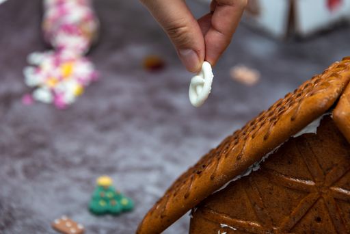 A closeup shot of a hand putting a candy on a gingerbread house roof